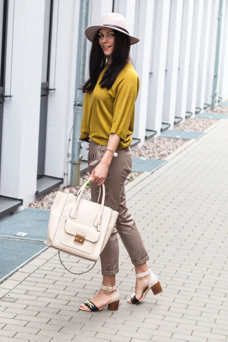 Kleidermädchen präsentiert ein Outfit in Beige und Gelb für den Frühling. Sie trägt Hose und Sandalen von River Isalnd, Tasche von Clarks, Hut und Pullover von H&M und Armreif von Zara.