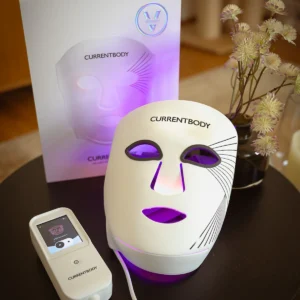 CurrentBody LED-Maske der 3. Generation mit Controller und Verpackung auf einem Beistelltisch.