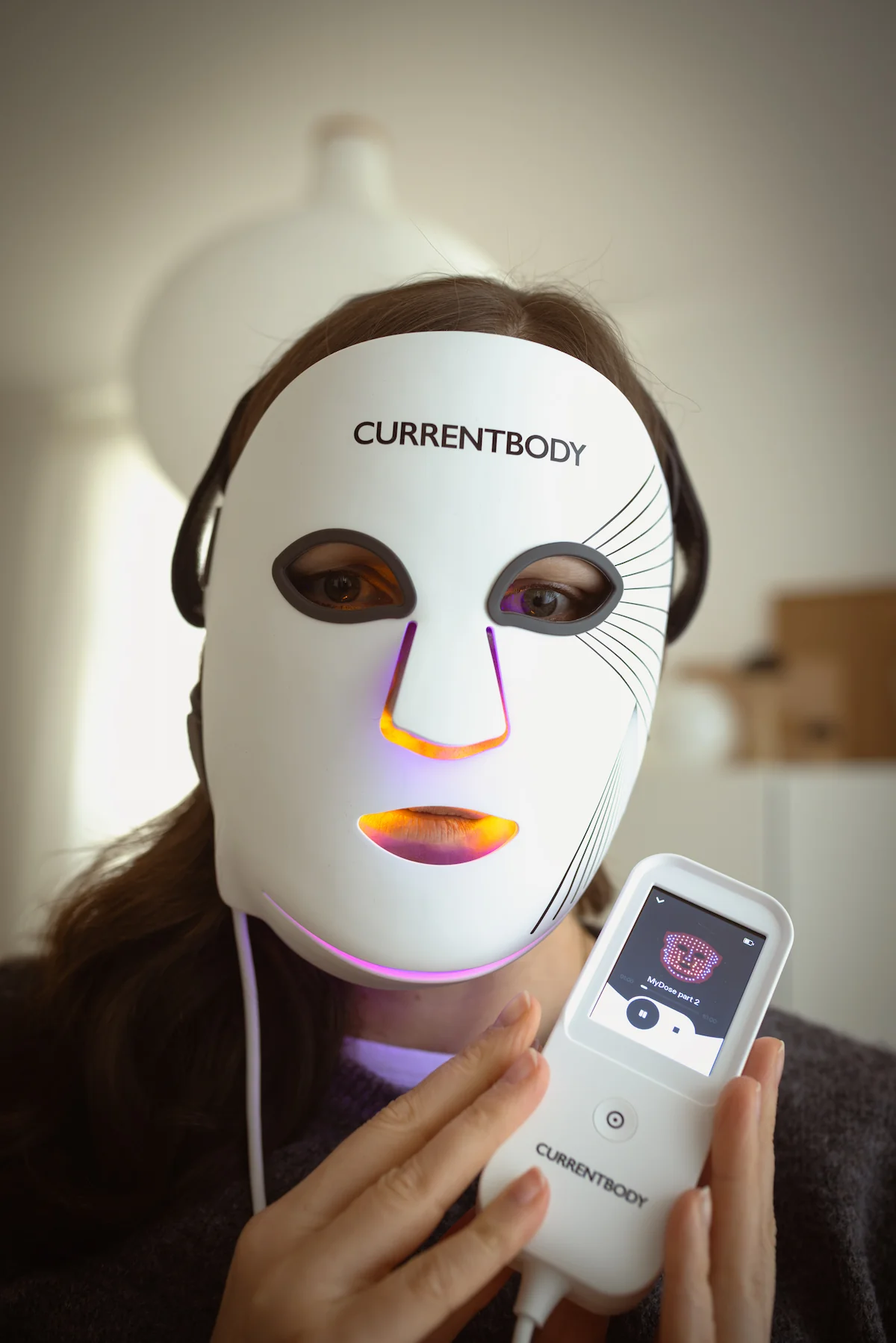 Jessika trägt die CurrentBody LED-Maske der 3. Generation und hält den Controller mit laufendem MyDose-Programm.